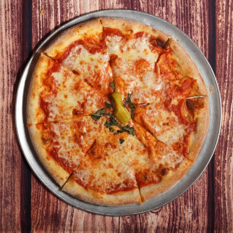 A Billito's Italian Restaurant cheese pizza, sliced, with a pepperoncini and basil on a metal pan.