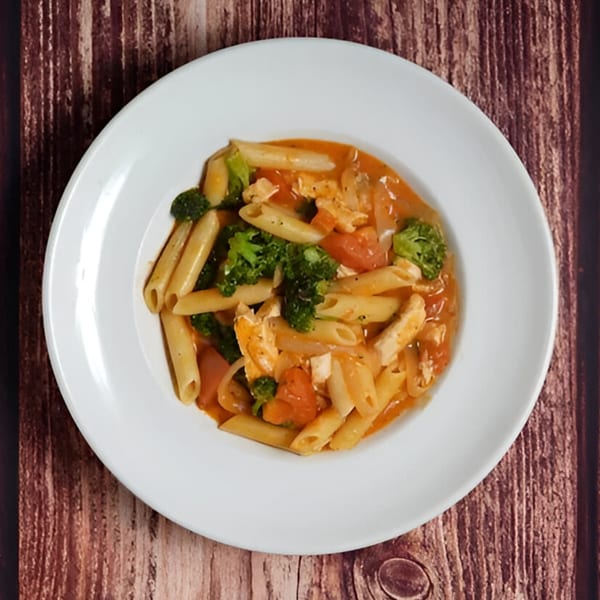 Penne pasta with chicken, broccoli, and tomatoes in a creamy orange sauce on a white plate.