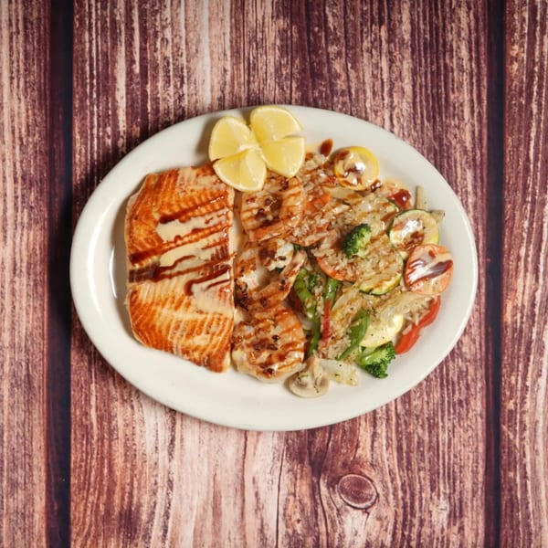 Grilled salmon and shrimp with rice and mixed vegetables, garnished with lemon wedges on a white plate.