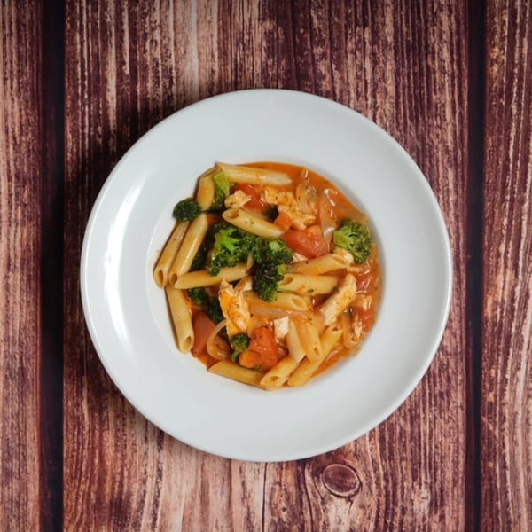 Penne pasta with chicken, broccoli, and tomatoes in a red sauce, served on a white plate.