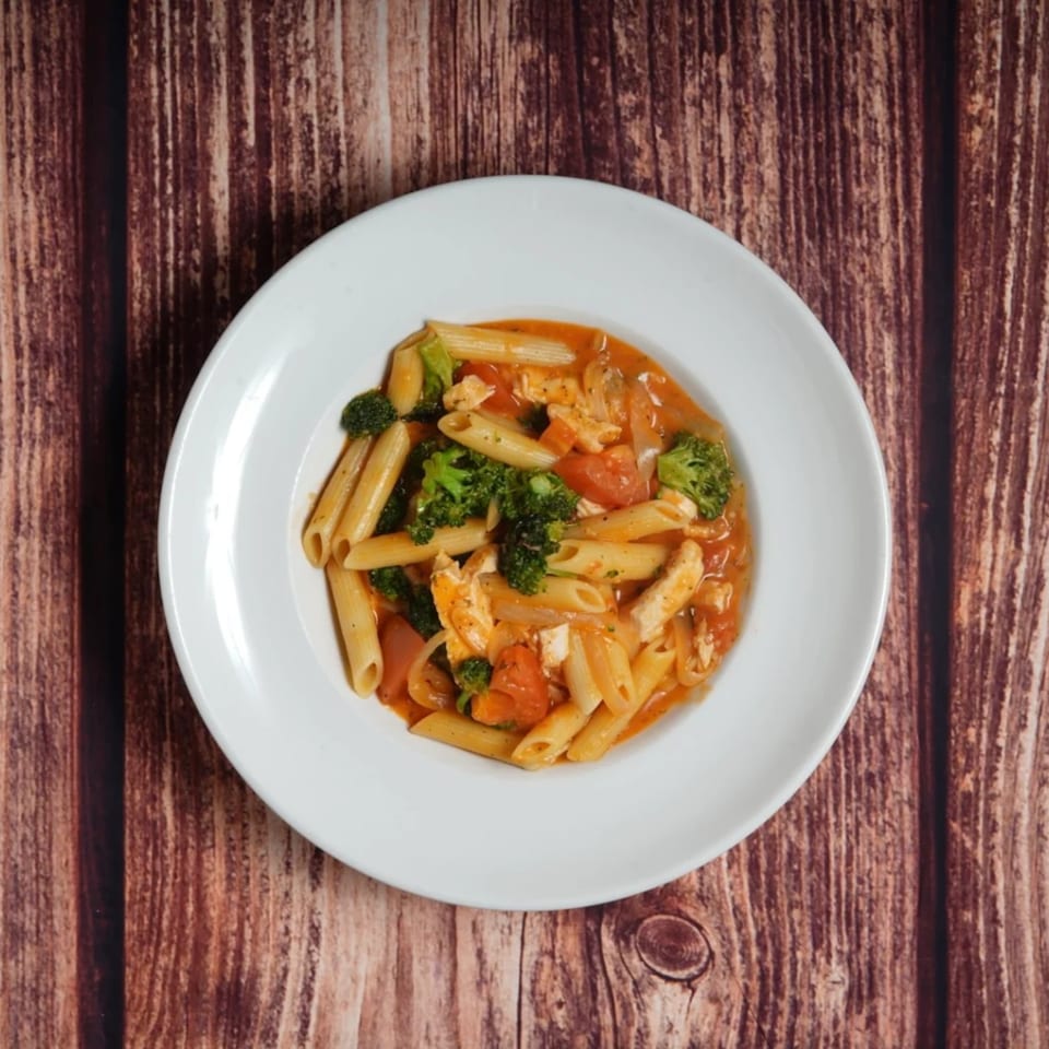 Penne pasta with chicken, broccoli, and tomatoes in a red sauce, served on a white plate.