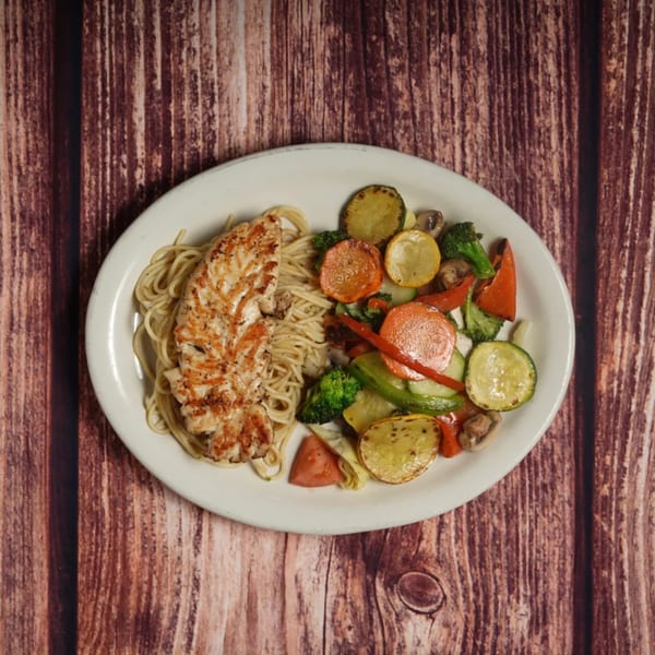 Grilled chicken breast with spaghetti and colorful roasted vegetables on a white plate.